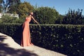 Beautiful mulatto girl with dark hair wears elegant coral dress with bijou ,posing beside antic palace