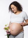 Beautiful multi ethnic gravid woman holding bunch of flowers, smiling looking at her pregnant belly in late pregnancy Royalty Free Stock Photo