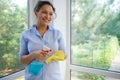 Beautiful woman housewife spraying detergent on a yellow cloth while washing windows in veranda. Spring cleaning concept