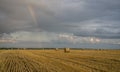 Beautiful multicolored rainbow over a sloping wheat field with large rolls of straw