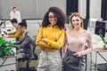 Beautiful multiethnic businesswomen standing and smiling at camera while colleagues working behind Royalty Free Stock Photo