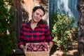 Beautiful woman in a red plaid shirt holding a wooden box with harvested organic potatoes grown in a summer cottage