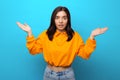 Beautiful multiethnicity woman in orange trendy shirt surprised expression against blue background