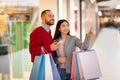 Beautiful multiracial couple with paper bags using smartphone to make online order or shopping list at city mall Royalty Free Stock Photo