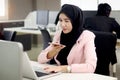 Beautiful Muslim Asian woman officer with hijab, talking with customer by mobile phone while working on laptop computer at office Royalty Free Stock Photo