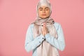 Muslim girl in hijab praying with closed eyes, isolated on pink