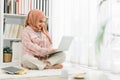 Beautiful Muslim girl wearing a hijab is working with a laptop computer at home, sitting on the floor in the living room Royalty Free Stock Photo