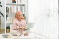 Beautiful Muslim girl wearing a hijab is working with a laptop computer at home, sitting on the floor in the living room Royalty Free Stock Photo