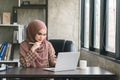 A beautiful Muslim millennial Asian businesswoman wearing a brown hijab working remotely from her home office. Royalty Free Stock Photo