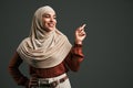 Beautiful muslim woman in beige hijab pointing finger at space on gray background. Copy space