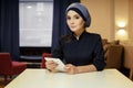 Beautiful Muslim woman in Islamic clothes sitting at a table with an electronic tablet in her hands