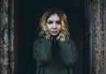 A mysterious blonde woman in a vintage sweater with a sad look stands in the doorway of an old abandoned creepy house. Horror and Royalty Free Stock Photo