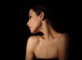 Beautiful mysterious woman in darkness with healthy neck and golden health skin in shadows on dramatic black background with