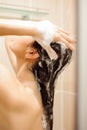 Beautiful naked young woman using shampoo while taking shower in bathroom. Royalty Free Stock Photo