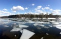 Natural landscape with ice floes adrift on the spring river and forest trees on opposite bank under clouds on blue sky reflected i Royalty Free Stock Photo