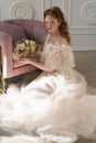 Beautiful natural redhead girl bride, with nude makeup, wearing a white dress, holds a wedding bouquet in her hands and sits on Royalty Free Stock Photo