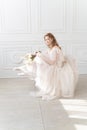 Beautiful natural redhead girl bride, with nude makeup, wearing a white dress, holds a wedding bouquet in her hands and sits on at Royalty Free Stock Photo