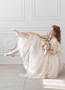 Beautiful natural redhead girl bride, with nude makeup, wearing a white dress, holds a wedding bouquet in her hands and sits on at Royalty Free Stock Photo