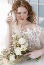 Beautiful natural redhead girl bride, with nude makeup, wearing a white dress, holds a wedding bouquet in her hands, sitting in Royalty Free Stock Photo