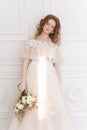 Beautiful natural redhead girl bride, with nude makeup, wearing a white dress, holds a wedding bouquet in her hands, standing an Royalty Free Stock Photo
