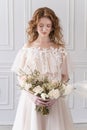 Beautiful natural redhead girl bride, with nude makeup, wearing a white dress, holds a wedding bouquet in her hands, standing in a Royalty Free Stock Photo