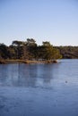 Beautiful natural Scandinavian landscape. Frozen lake with forest and stones at the shore line. Sunny late autumn or winter day in Royalty Free Stock Photo