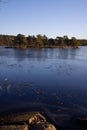 Beautiful natural Scandinavian landscape. Frozen lake with forest and stones at the shore line. Sunny late autumn or winter day in Royalty Free Stock Photo