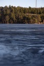 Beautiful natural Scandinavian landscape. Frozen lake with forest and stones at the shore line. Sunny late autumn or winter day in Royalty Free Stock Photo