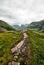 Path over green pasture in the mountains of Western Norway with snow on the summits and a dark cloudy sky Royalty Free Stock Photo