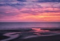 Beautiful near dark twilight over a calm flat sea with purple sky and blue clouds reflected in water on the beach Royalty Free Stock Photo