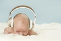 Little beautiful newborn baby in big headphones listening to music, isolated on blue background