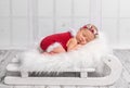 Beautiful newborn in red romper on sleigh cot