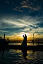 Beautiful newlyweds on the background of the Bay, beautiful sky and clouds. Silhouettes of bride and groom on the pier in the rays Royalty Free Stock Photo