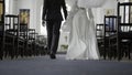 Beautiful newlyweds walking down aisle. Action. Rear view of couple of newlyweds in church. Newlyweds walk down aisle at