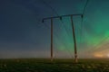 Beautiful night Aurora over double wooden pole power lines in autumn field, front view, starry sky with Aurora Borealis. Sweden,