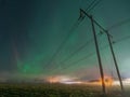 Beautiful night Aurora over double wooden pole power lines and electrical substation in autumn field, side view, starry sky with