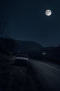 Beautiful night landscape of big full moon rising over the mountain road with hill and trees, with car near road Royalty Free Stock Photo