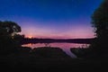 Beautiful night landscape on the forest lake with stars and reflected clouds in water in spring. Colorful sky. Nature background