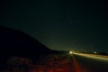Beautiful night landscape of stars at sky and mountain silhouette near road with car trails. Road in the mountains under a starry Royalty Free Stock Photo
