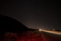 Beautiful night landscape of stars at sky and mountain silhouette near road with car trails. Road in the mountains under a starry Royalty Free Stock Photo