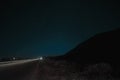 Beautiful night landscape of stars at sky and mountain silhouette near road with car trails. Road in the mountains under a starry Royalty Free Stock Photo