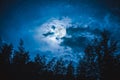 Beautiful night sky with many stars and full moon behind partial cloudy above silhouettes of trees. Serenity nature background.