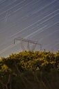 Beautiful night view of falling Lyrid meteors, star trails, power lines, electric transmission pylon and yellow flowering gorse Royalty Free Stock Photo