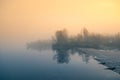 A beautiful Norwegian autumn scenery. Misty morning on a lake. Water flowing over the dam, waterfall. Royalty Free Stock Photo