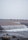 A beautiful Norwegian autumn scenery. Misty morning on a lake. Water flowing over the dam, waterfall. Royalty Free Stock Photo