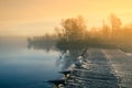 A beautiful Norwegian autumn scenery. Misty morning on a lake. Water flowing over the dam, waterfall. Royalty Free Stock Photo