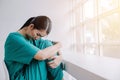 A beautiful nurse hugging her knees in a chair with a sad and worried expression, unhappy at work concept Royalty Free Stock Photo