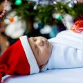 Beautiful one week old newborn baby wrapped in blanket near Christmas tree with colorful garland lights on background Royalty Free Stock Photo