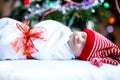 Beautiful one week old newborn baby wrapped in blanket near Christmas tree with colorful garland lights on background Royalty Free Stock Photo