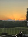 Beautiful Orange Sunset Behind Fluffy Clouds Behind Treeline with Fence and Firepit in Foreground Royalty Free Stock Photo
